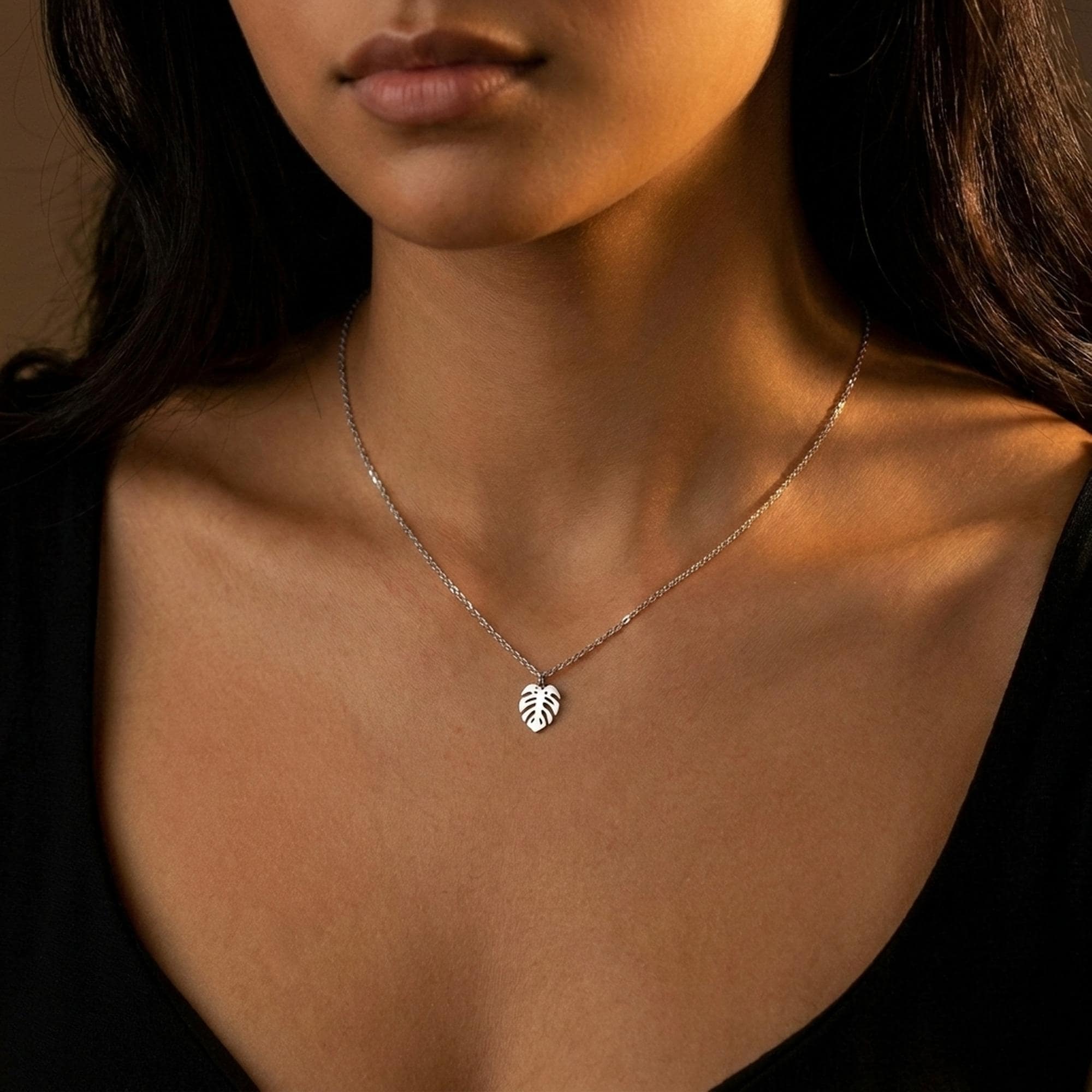 Fine gold chain necklace with a small split monstera leaf pendant on a plain background (2 of 8)