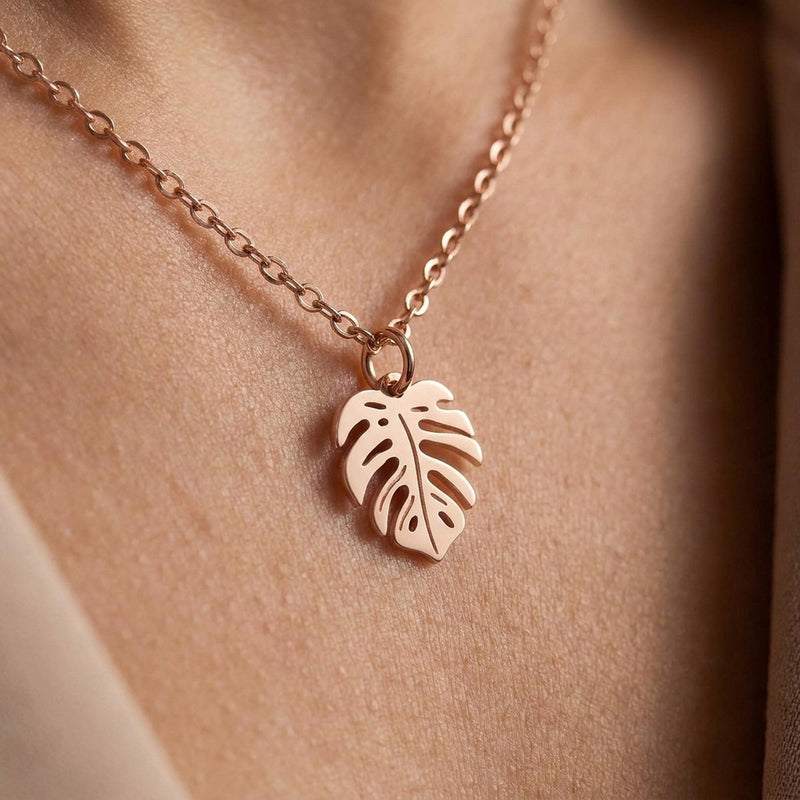 Fine gold chain necklace with a small split monstera leaf pendant on a plain background (3 of 8)