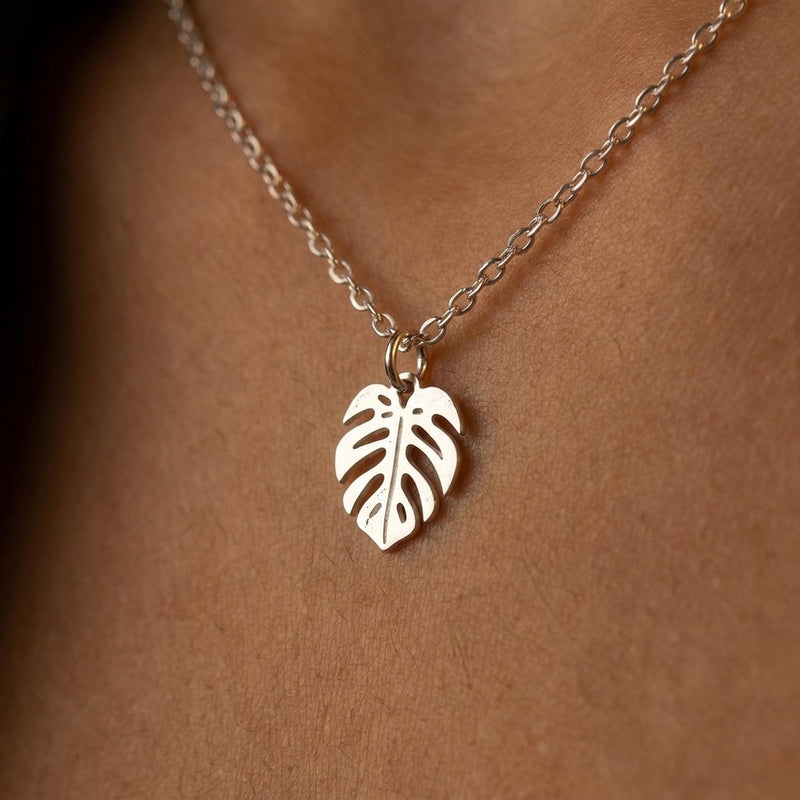 Fine gold chain necklace with a small split monstera leaf pendant on a plain background (4 of 8)