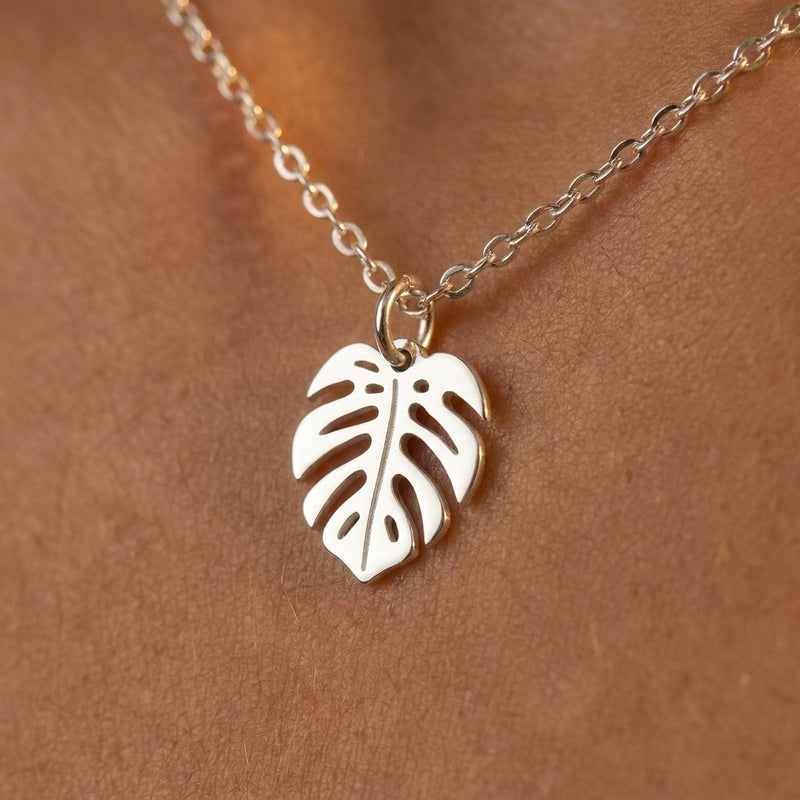 Fine gold chain necklace with a small split monstera leaf pendant on a plain background (5 of 8)