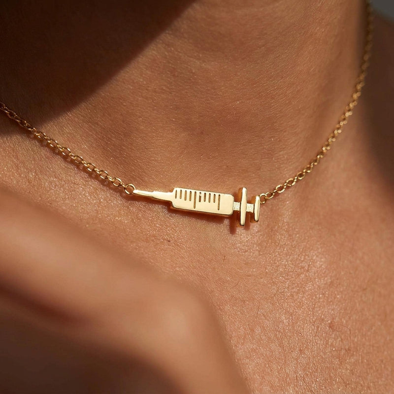 Slim gold syringe pendant with plunger and needle hanging from a thin chain (2 of 9)