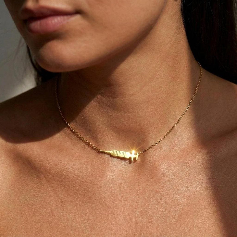 Slim gold syringe pendant with plunger and needle hanging from a thin chain (3 of 9)