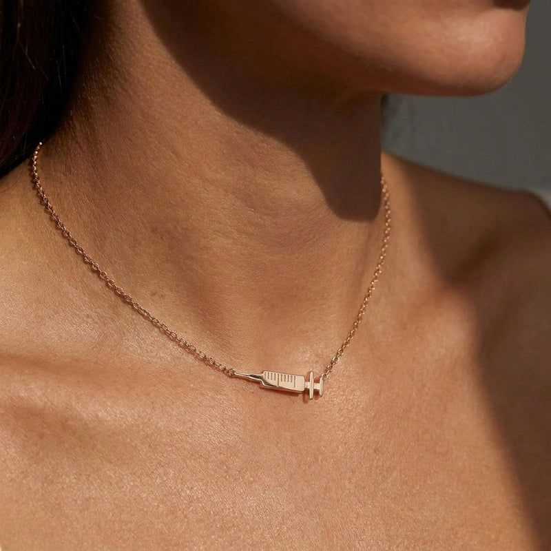Slim gold syringe pendant with plunger and needle hanging from a thin chain (5 of 9)