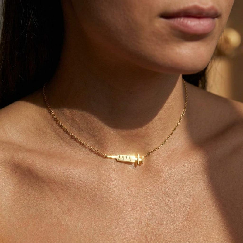 Slim gold syringe pendant with plunger and needle hanging from a thin chain (6 of 9)