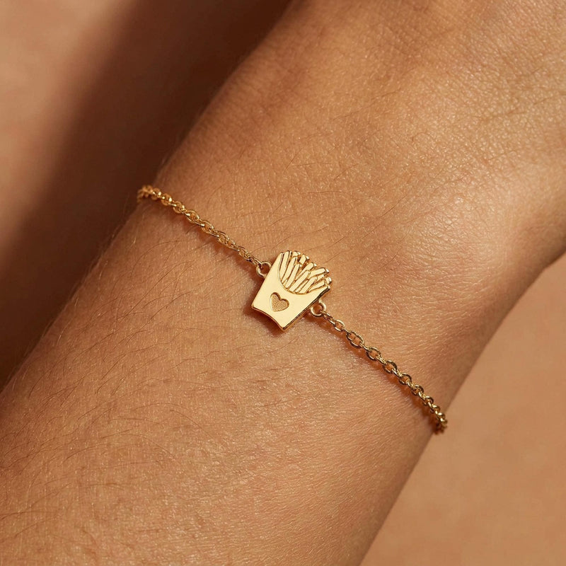 Fine gold chain bracelet with a tiny carton of french fries charm, on white