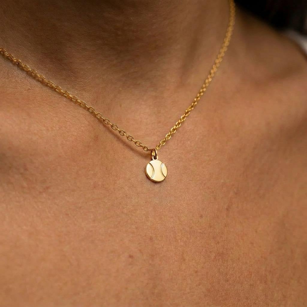 Fine gold cable chain necklace with a tiny tennis ball pendant with a curved seam