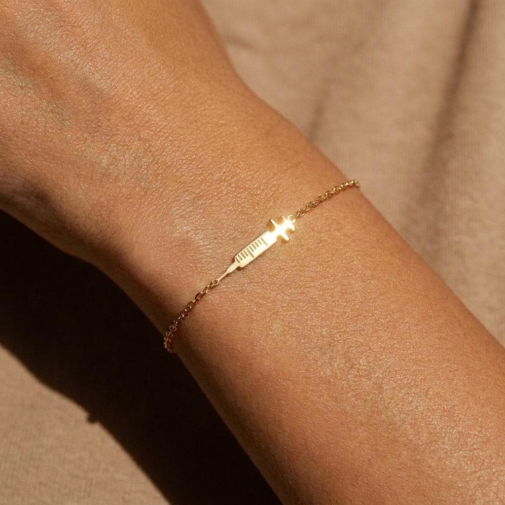 Fine cable chain bracelet with a flat gold syringe charm marked with measurement lines.