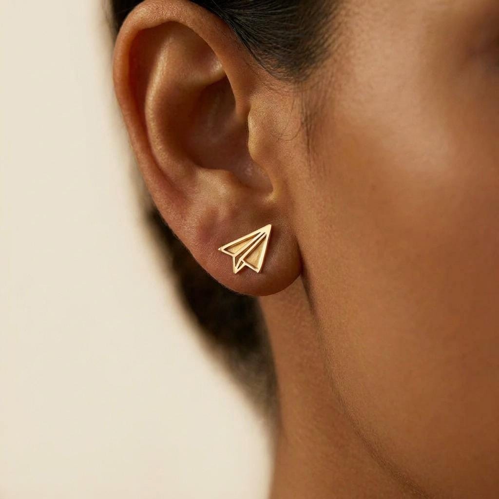 Tiny gold paper airplane stud earrings with cut fold lines, shown as a pair