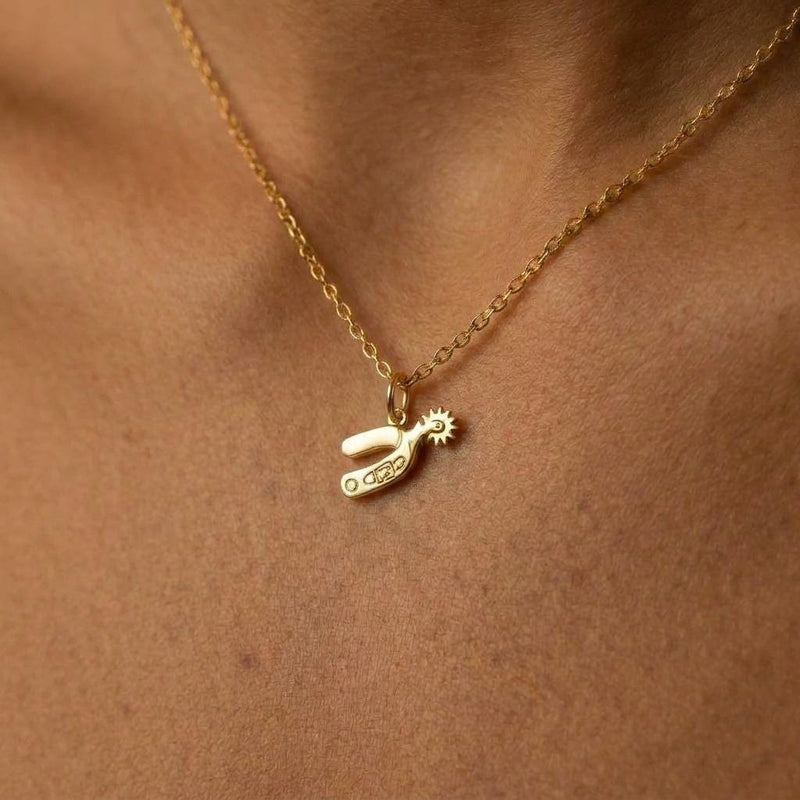 Small gold cowboy spur pendant with rowel hanging from a thin cable chain