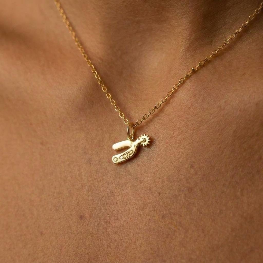 Small gold cowboy spur pendant with rowel hanging from a thin cable chain