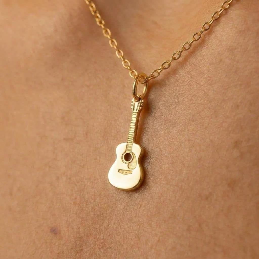 Tiny gold acoustic guitar pendant on a fine cable chain against a white background.