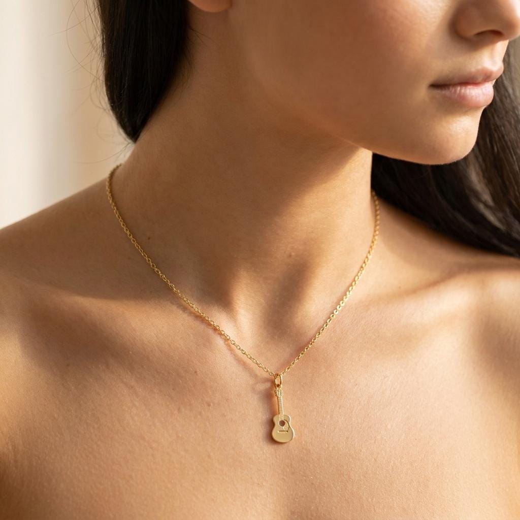 Tiny gold acoustic guitar pendant on a fine cable chain against a white background. (2 of 9)