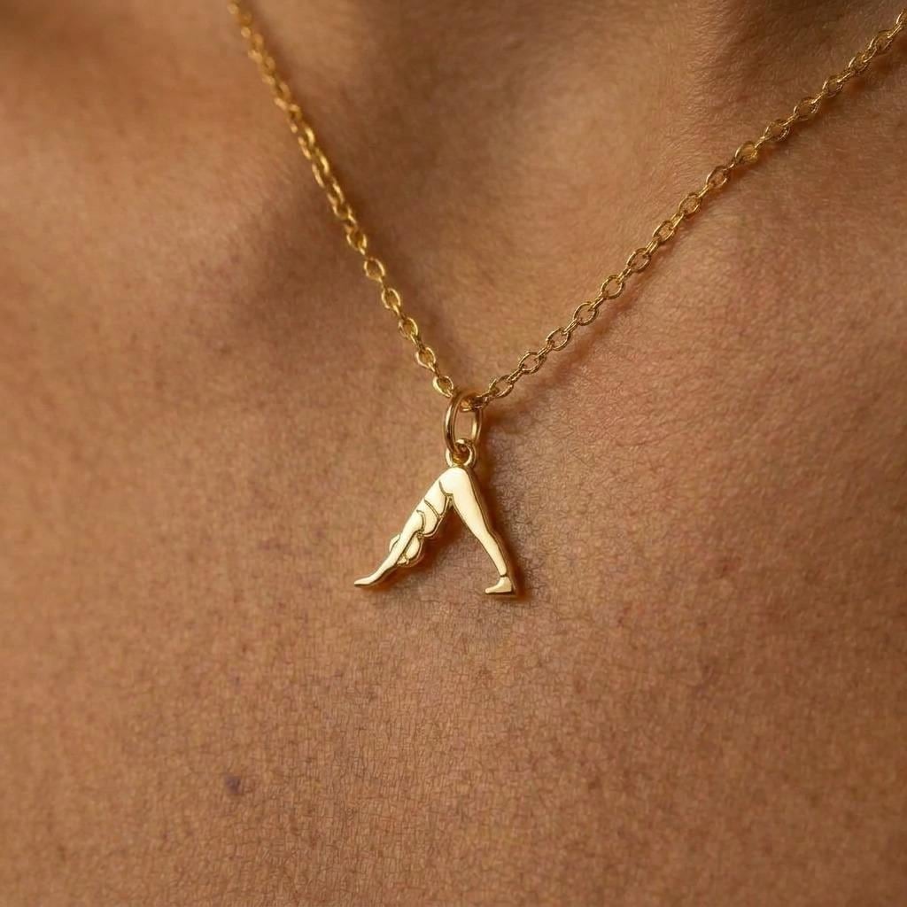 Small gold pendant of a figure in downward dog pose on a fine chain, white background.