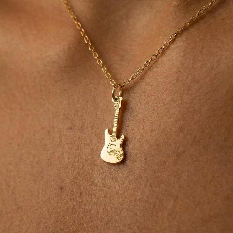 Tiny gold electric guitar pendant hanging from a fine cable chain on a white background.
