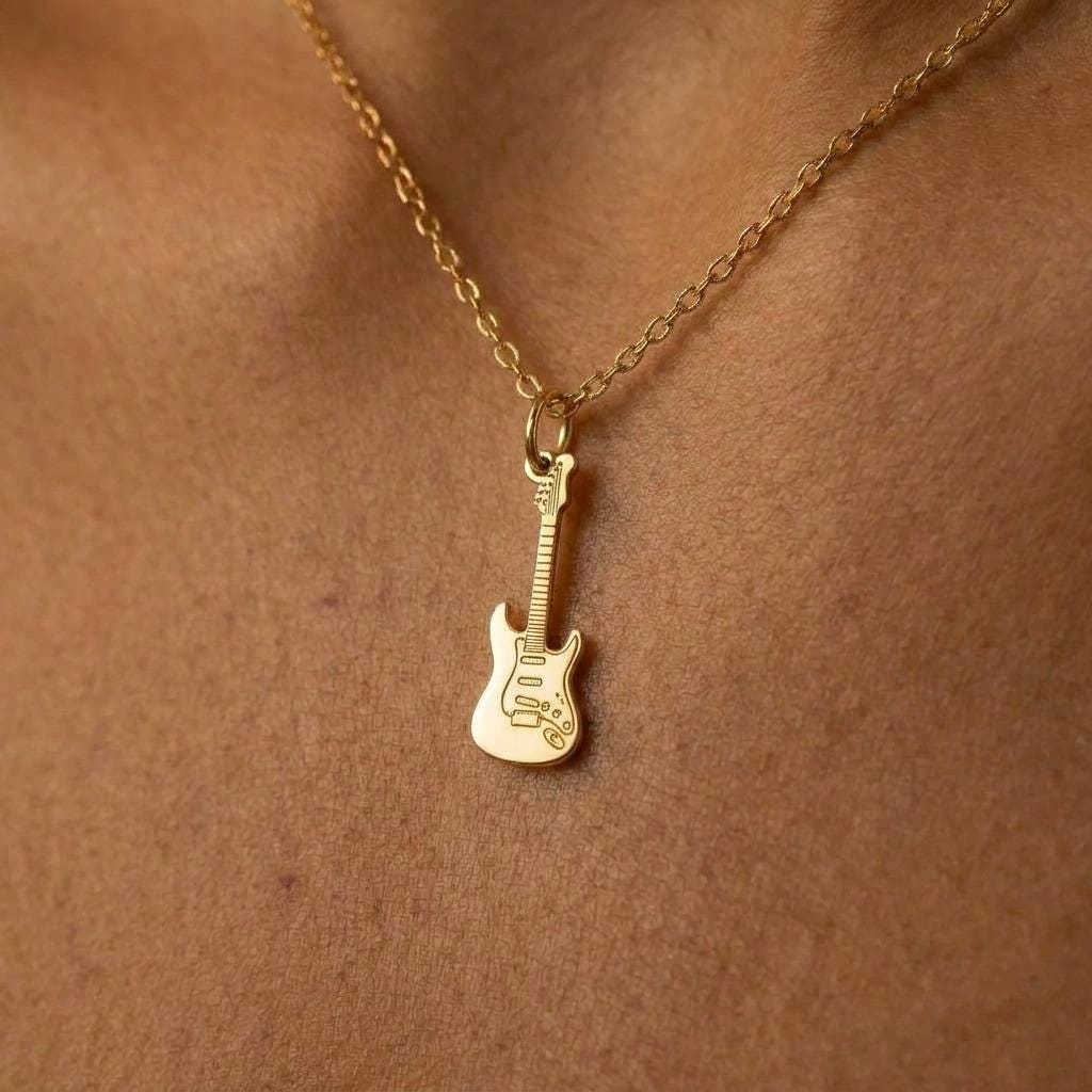 Tiny gold electric guitar pendant hanging from a fine cable chain on a white background.