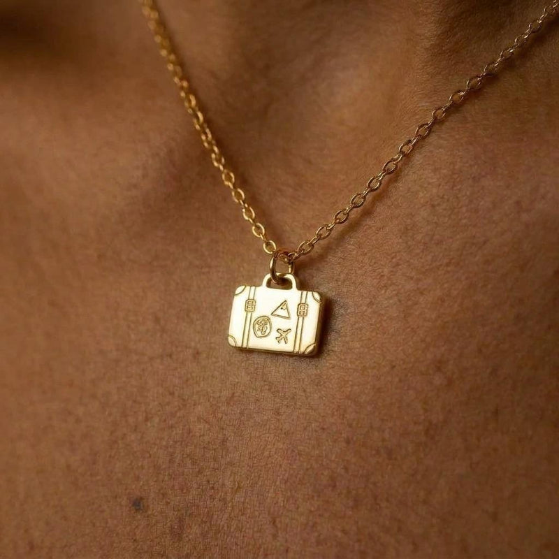 Small gold suitcase pendant with top handle and front clasps on a thin chain