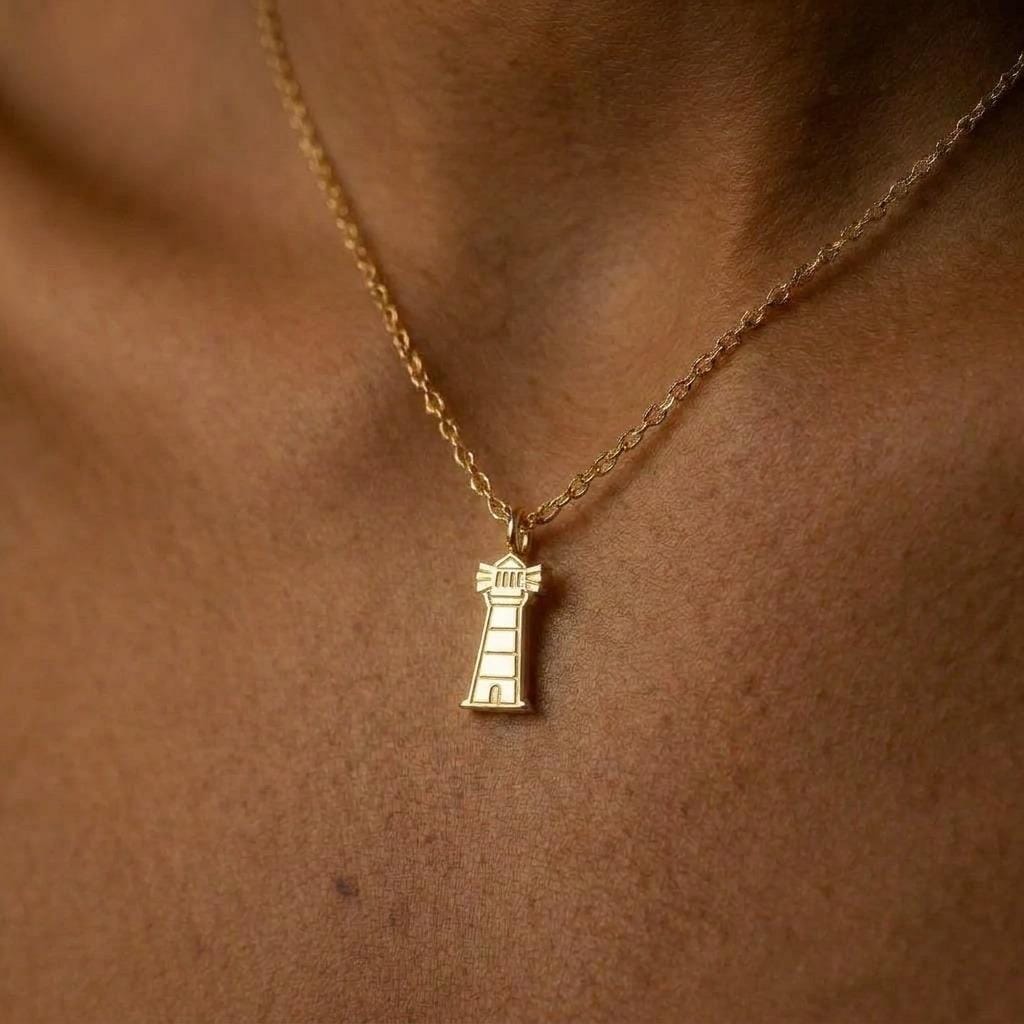 Small gold lighthouse pendant on a fine cable chain against a white background.