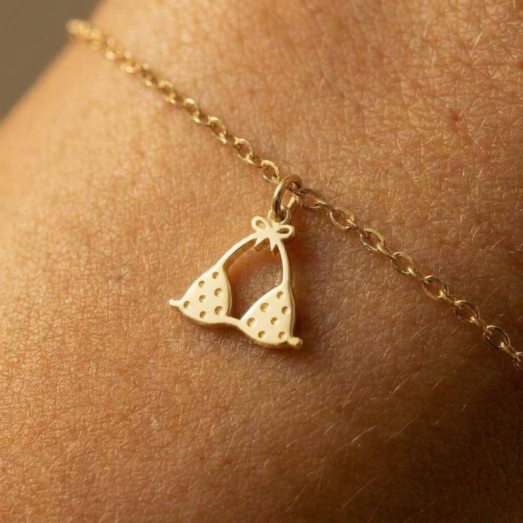 Tiny gold bikini charm on a delicate bracelet chain with clasp, white background.