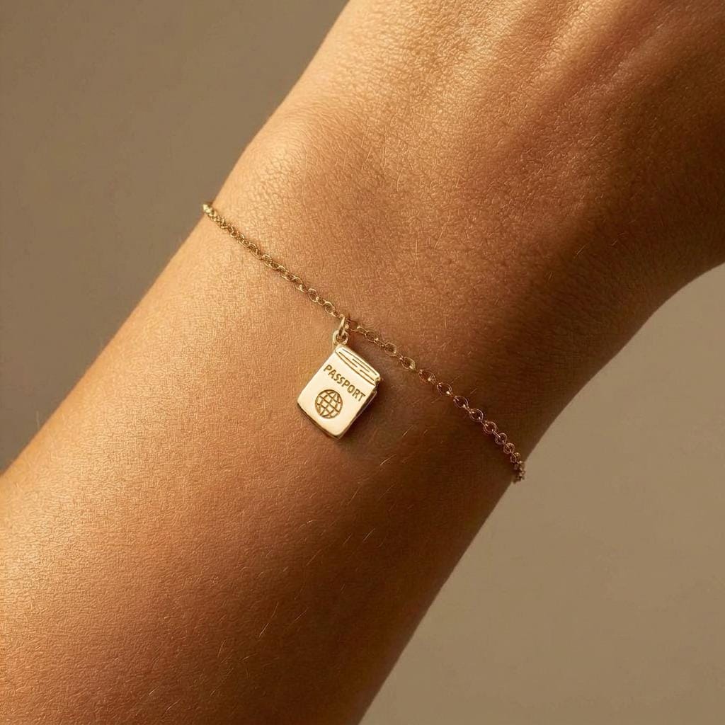 Tiny gold passport charm on a fine bracelet chain with clasp, white background.