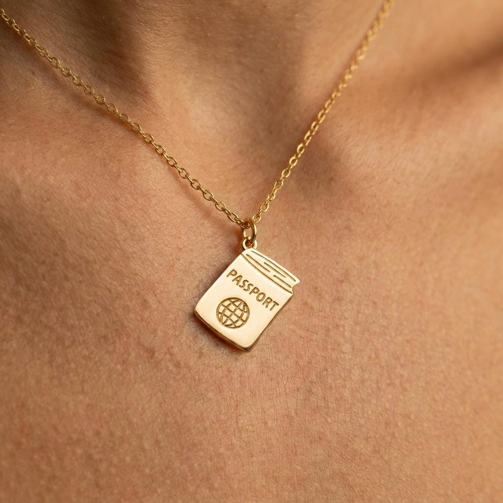Tiny gold passport pendant on a fine cable chain against a white background.