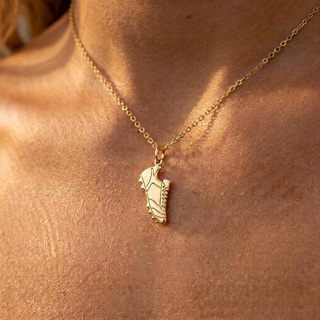 Small gold soccer cleat pendant hanging from a fine gold chain on a white background (2 of 8)