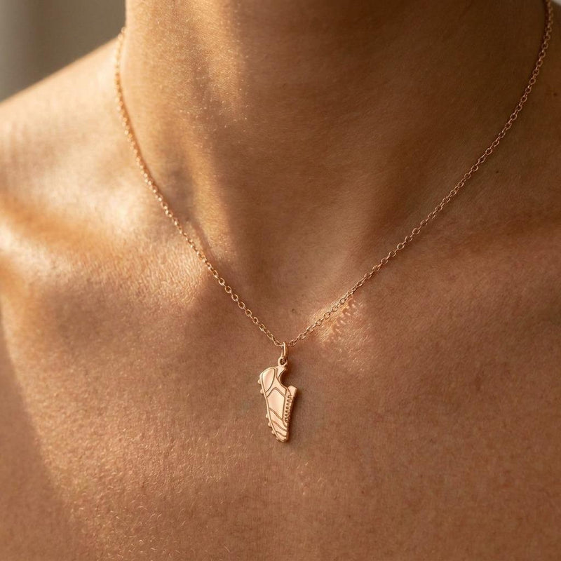 Small gold soccer cleat pendant hanging from a fine gold chain on a white background (4 of 8)