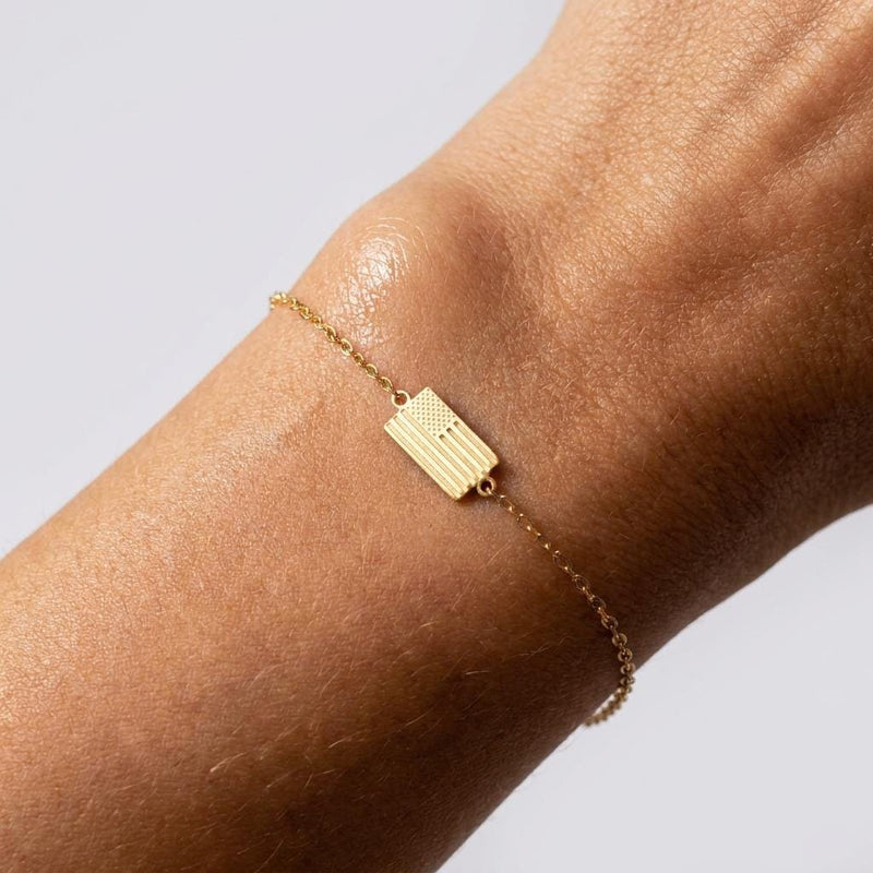 Tiny gold American flag charm with cut stripes and a star field on a fine chain bracelet