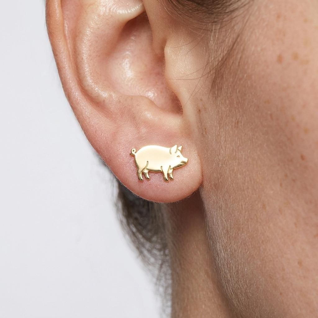Pair of small pig stud earrings in gold shown in profile with a curled tail (2 of 5)