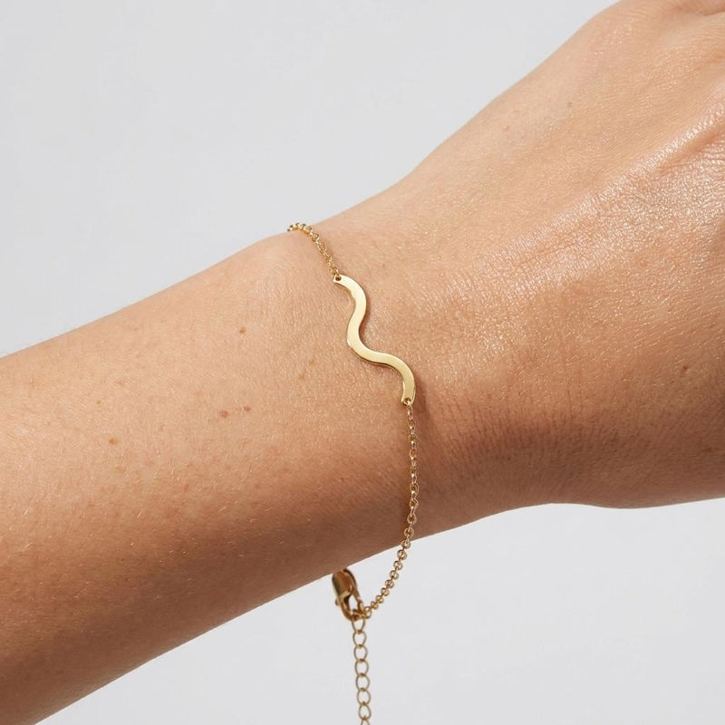 Gold bracelet with a winding river charm on a fine wave link chain