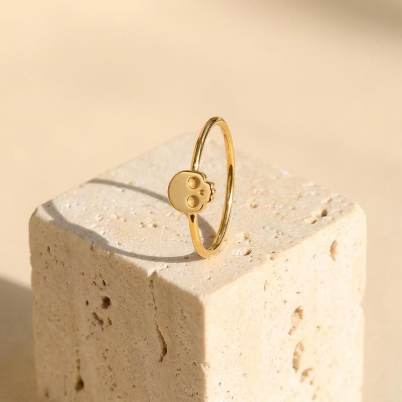 Thin gold ring set with a small skull charm with cut eye sockets and a grin
